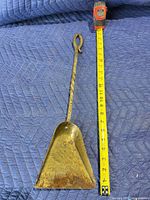 Front of brass fireplace shovel with tape measure showing length