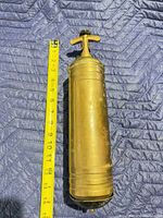 front view of brass fire extinguisher beside tape measure