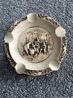 Front view of stoneware ashtray showing four rests, scroll border, central tavern relief