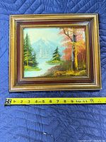 Front view of framed oil landscape painting with tape measure showing width