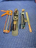 Group shot of caulk gun, bench plane, surform rasp plane, and file on padded surface