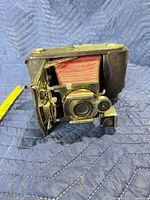 Front three-quarter view of Kodak folding bellows camera showing red bellows, leather covering and lens assembly