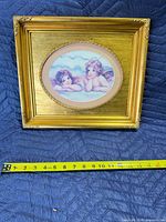 Front view showing cherub print and gilt frame with tape measure for scale