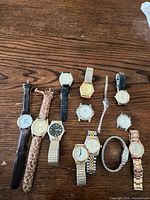 Overview of thirteen assorted wrist watches laid out on wooden surface