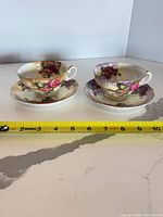 Side view of two teacups on saucers with measuring tape for scale