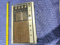 Front view showing speaker grille, control panel, knobs and measuring tape indicating length