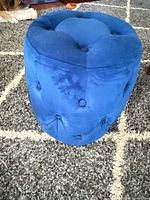 Full view of blue round velvet ottoman showing tufted sides and padded top