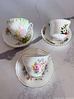 Three teacups on matching saucers showing patterns and gold trim