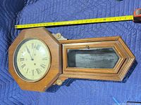 Front view of wooden schoolhouse regulator wall clock showing dial and glass lower door with tape measure for height reference