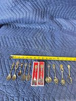 Front view of all 12 spoons beside ruler showing 4–5 in length