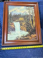 Front view of framed oil landscape painting with measuring tape showing height