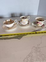 All three cup-and-saucer sets side by side with tape measure for scale