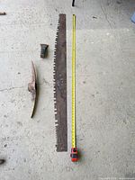 Overview of saw blade, pick mattock head, axe/adze head with tape measure for scale