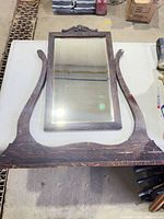Front view of mirror frame, glass, and detached curved supports/base on table