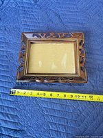 Front view showing carved wood frame with glass front and tape measure for scale