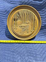 front view of round carved wood plaque with tape measure showing diameter