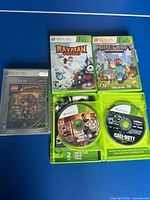 Five Xbox 360 game cases with open case showing discs