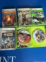 Five Xbox 360 games laid out on blue surface, one open case showing disc