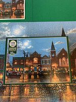 Box front on top of assembled puzzle showing artwork and Cobble Hill 1000-piece label