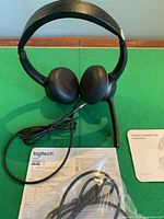 Headset front view showing ear cups, boom mic, attached cable, sealed spare cable bag, paperwork