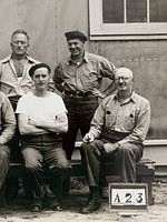 Front of photograph showing 11 internees and placard marked 62