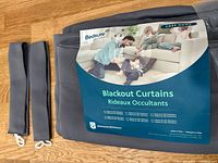 Folded gray blackout curtain set with packaging and two tiebacks visible