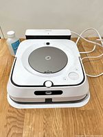 Robot mop seated on charging dock with power cable and cleaning solution bottle