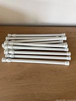Stack of white adjustable tension rods on wood surface