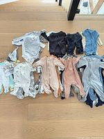 Grouped view of assorted baby onesies, sleepers and pants laid out on floor