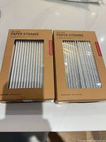 Front view of two unopened boxes of silver paper straws