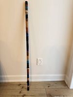 Full view of 4ft wood pole wrapped in multicolor leather leaning against wall