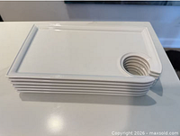 Stack of six identical white porcelain trays showing circular stem cut-out