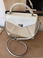 Front view of purse showing raffia body, white leather flap, gold flip-lock, strap