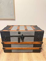 Front view of restored steamer trunk showing embossed gray metal panels, wood slats, black hardware