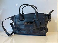 Full view of black Coach handbag showing overall design, handles, shoulder strap and hardware