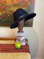 Side view of black wool felt fedora hat on display stand with apple for scale