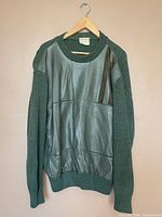 Green wool crewneck sweater with leather patchwork front on hanger