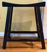 Side view of black wood stool showing legs and stretchers