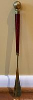 Full view of shoehorn front showing wood shaft and brass golf-ball finial