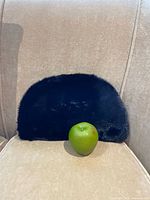 Front view of black otter fur hat with apple for scale