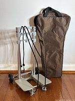 Folded cart standing beside brown nylon carrying case
