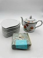 Stack of six white asymmetrical plates, floral teapot, sealed napkin pack