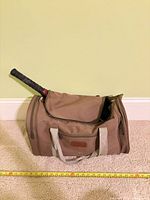 Brown duffel bag with paddle/racquet handle visible, measuring tape shows length