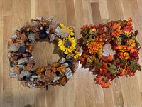 Both autumn wreaths side by side on wooden floor