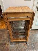 Full view of kitchen cart folded, showing drawer, three wire baskets and casters