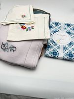 Stack showing packaged RockHill Home tablecloth, embroidered cream napkins and lavender linens