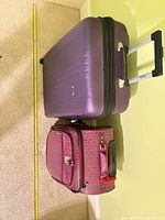 Large purple hardside suitcase and smaller plum patterned carry-on with measuring tape for scale