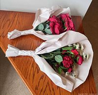 Two wrapped burgundy artificial flower bouquets on wooden surface