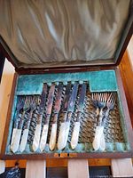 Open wooden box showing six knives and six forks in green velvet interior