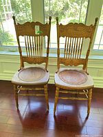 Front view of both solid oak pressed back dining chairs showing carved backs, seats, legs